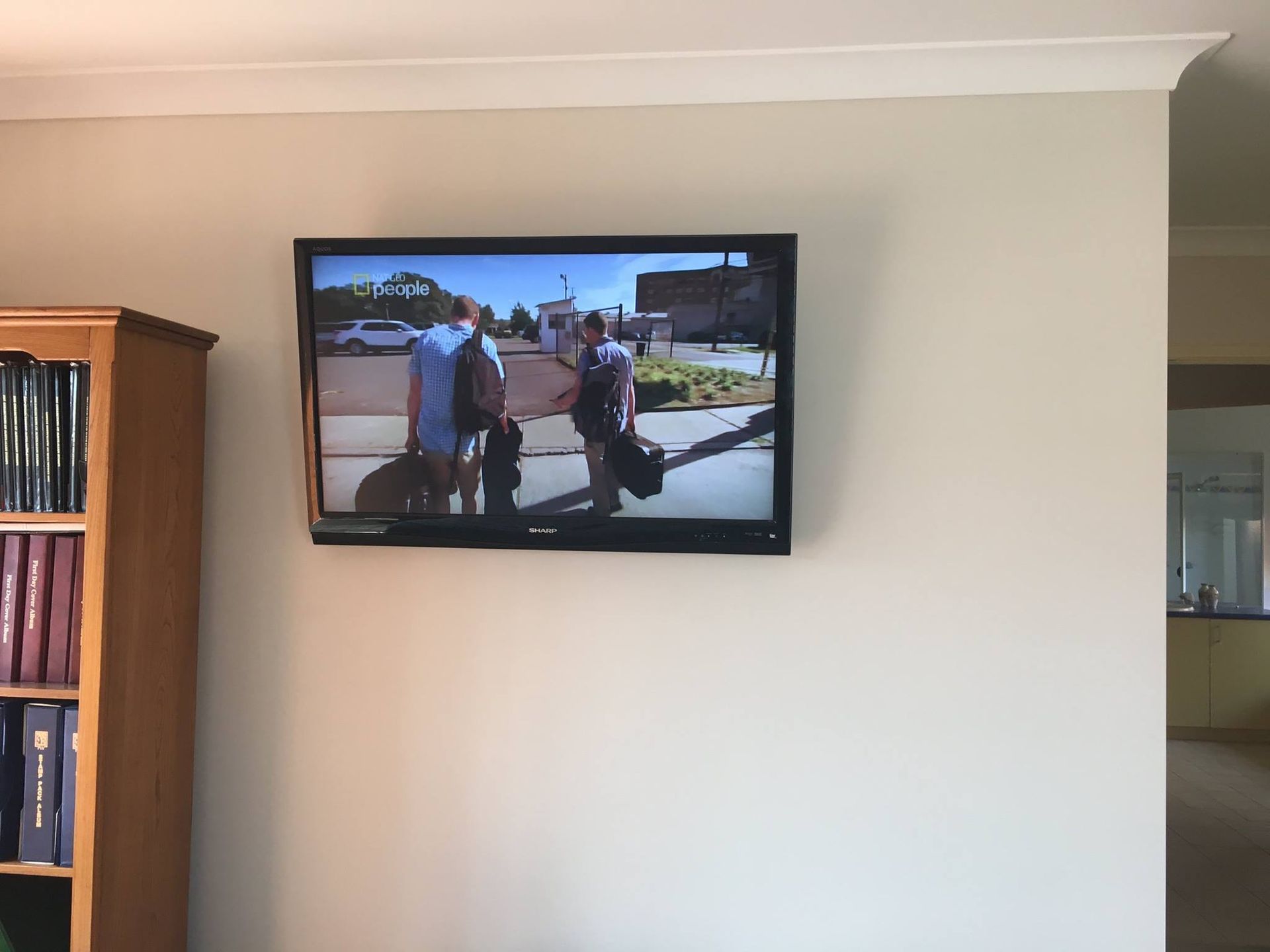 A TV Mounted on a Beige Wall, Showing People With Luggage Outside — BRC Antenna Service 1 In Banora Point, NSW