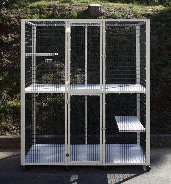 White wire cat enclosure with shelves, three compartments, and wheels, outdoors.