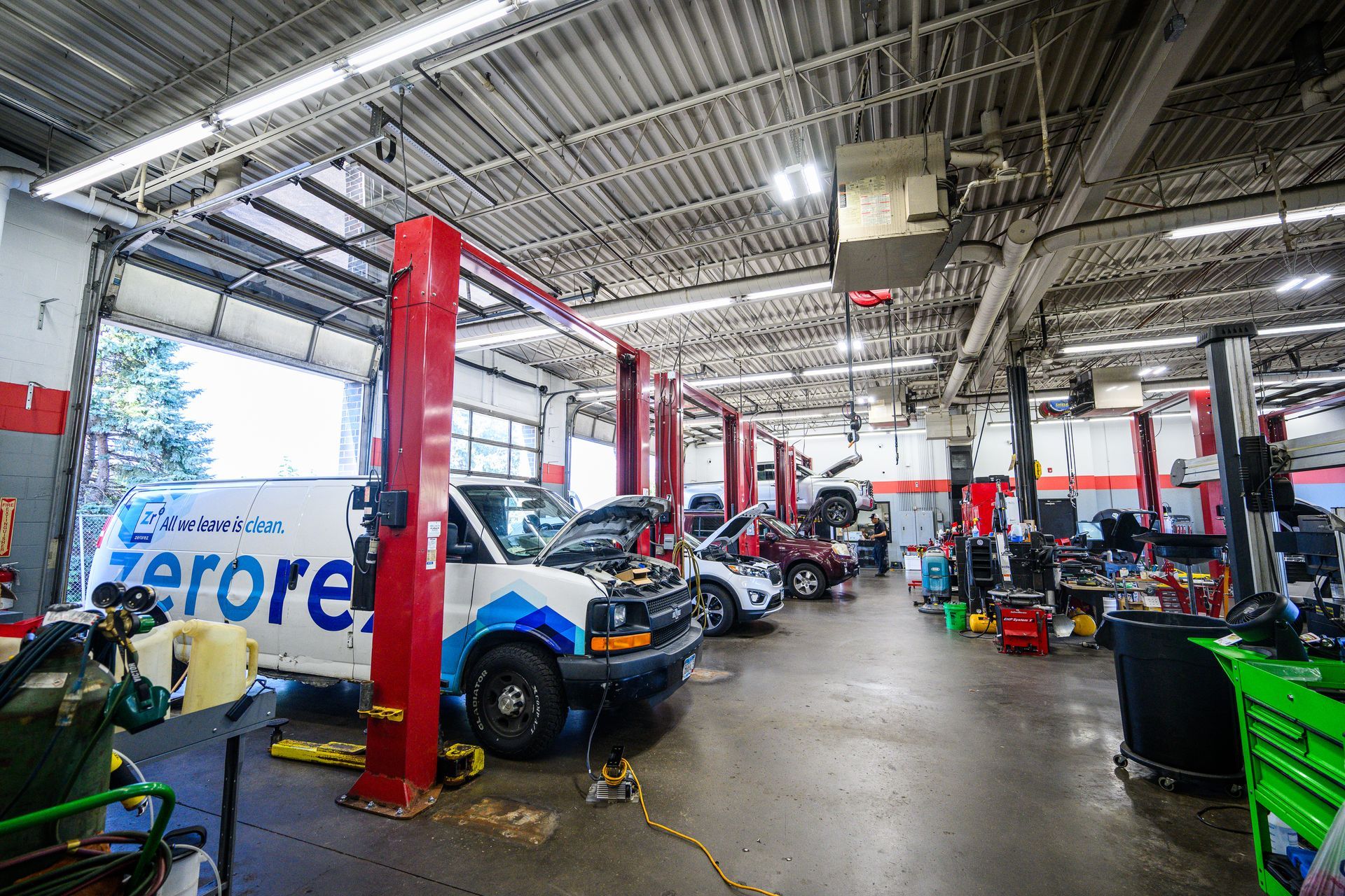 Auto repair shop interior. Vehicles on lifts, tools and equipment, open garage door, red and white accents.