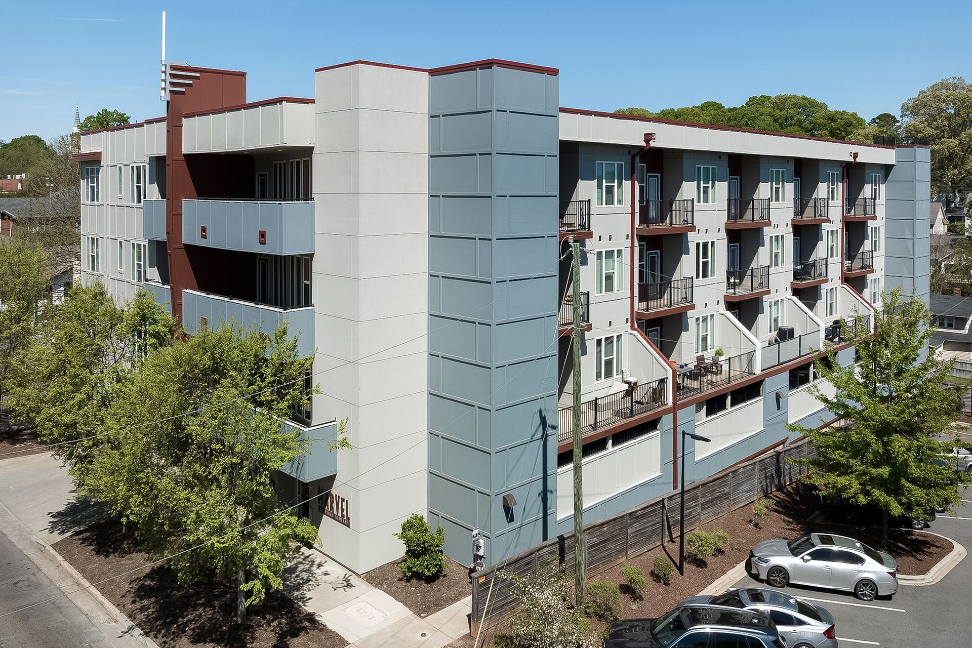 Modern apartment building with gray and white exterior, small balconies, and parked cars.