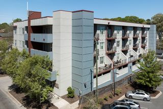 Modern apartment building with gray and white exterior, small balconies, and parked cars.