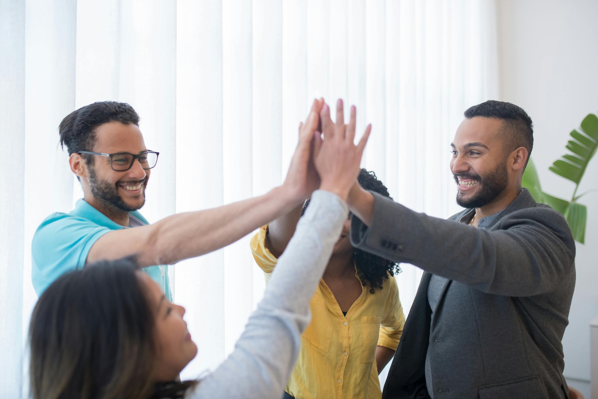 Team of four people high-fiving in a bright room, smiling.