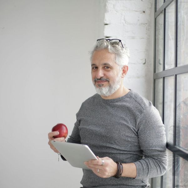 A man with a beard is holding an apple and a tablet.