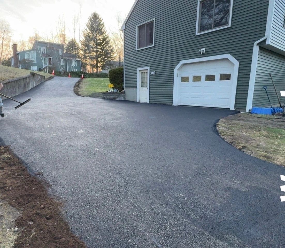 Newly paved asphalt driveway curves up to a green house with white garage door.