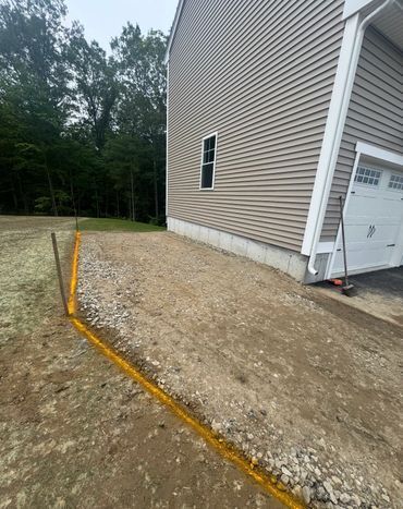 Gravel driveway next to a beige house. A yellow drainage pipe runs along the edge.