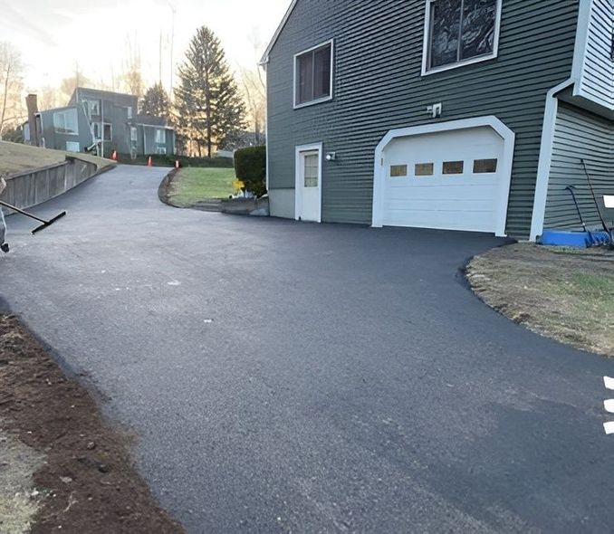 Newly paved asphalt driveway leading to a green house with a white garage door.