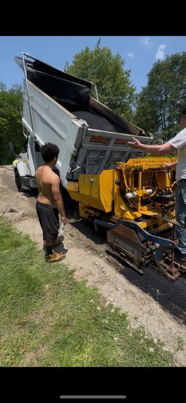 Men paving road with hot asphalt from a dump truck, sunny day.