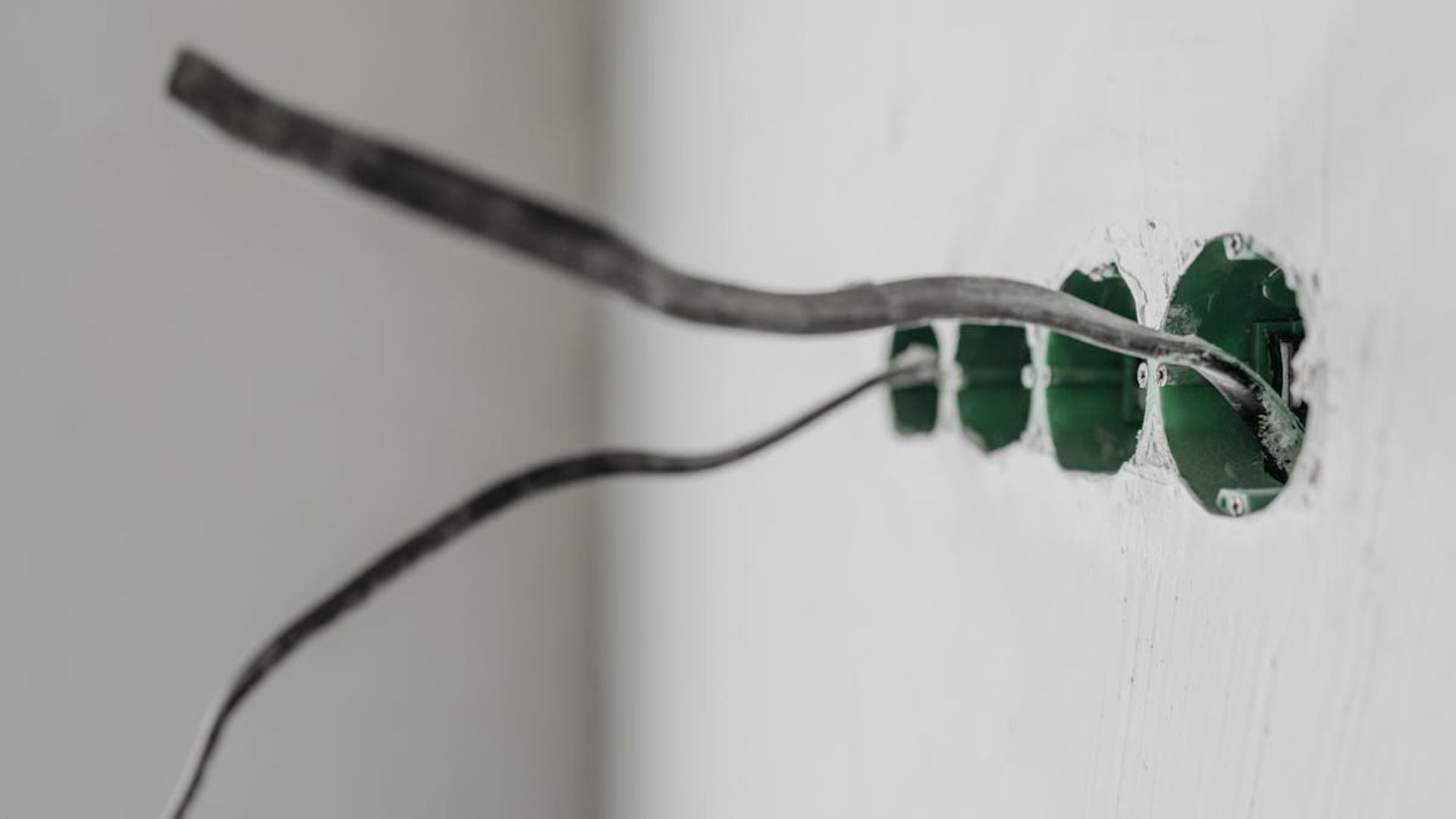 Cables eléctricos que sobresalen de insertos de plástico verde en una pared blanca.