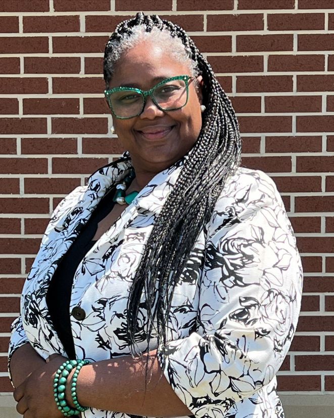 Julie A. Brown, recipient of the 2025 Betty J. Lewis Unsung Hero Scholarship at SAU Tech, standing in front of a brick wall in a floral blazer and green accessories.