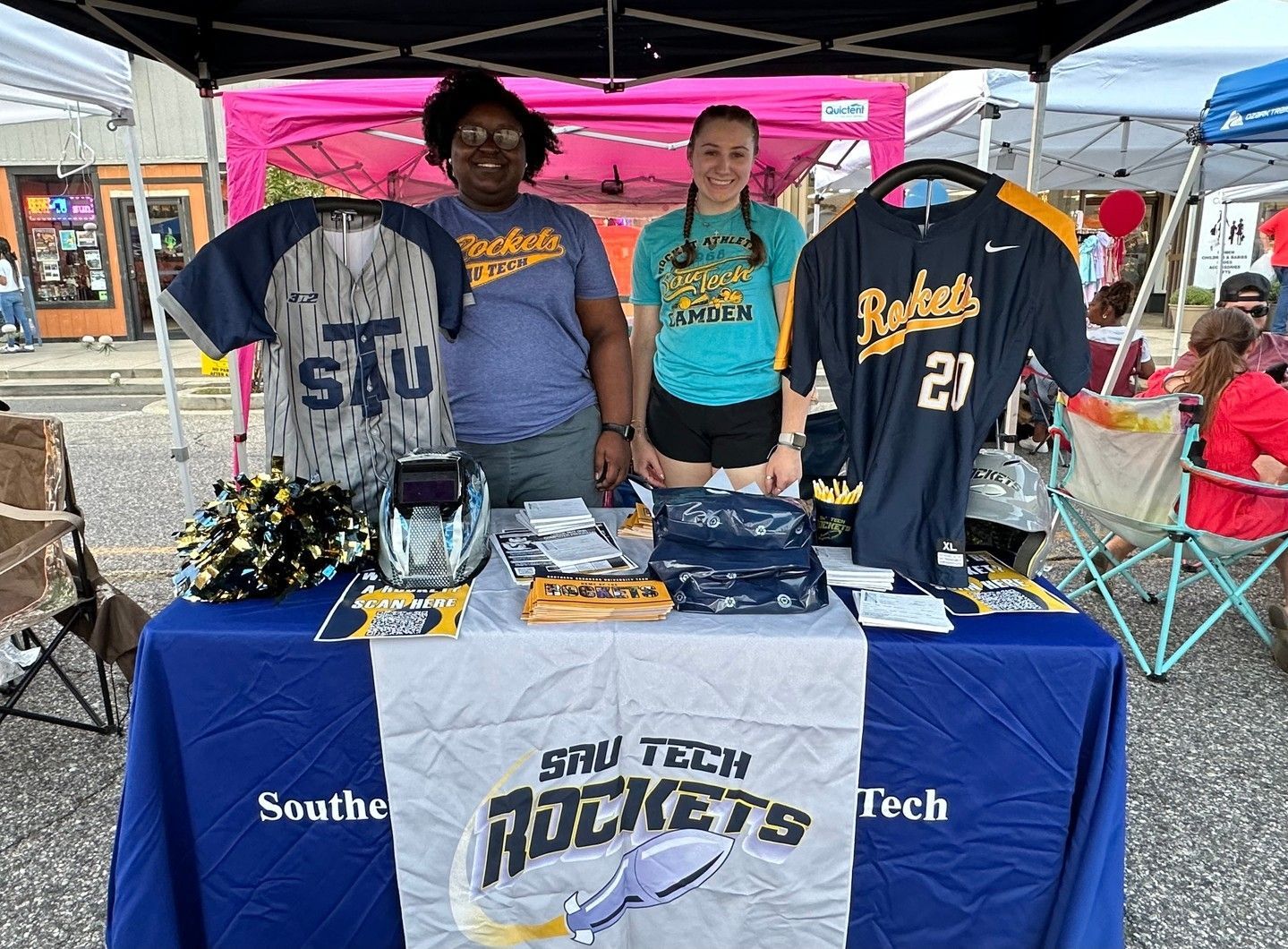 Two women are standing behind a table with shirts on it.