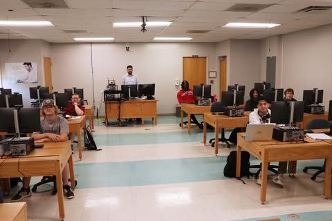 A group of people are sitting at desks in a computer lab.