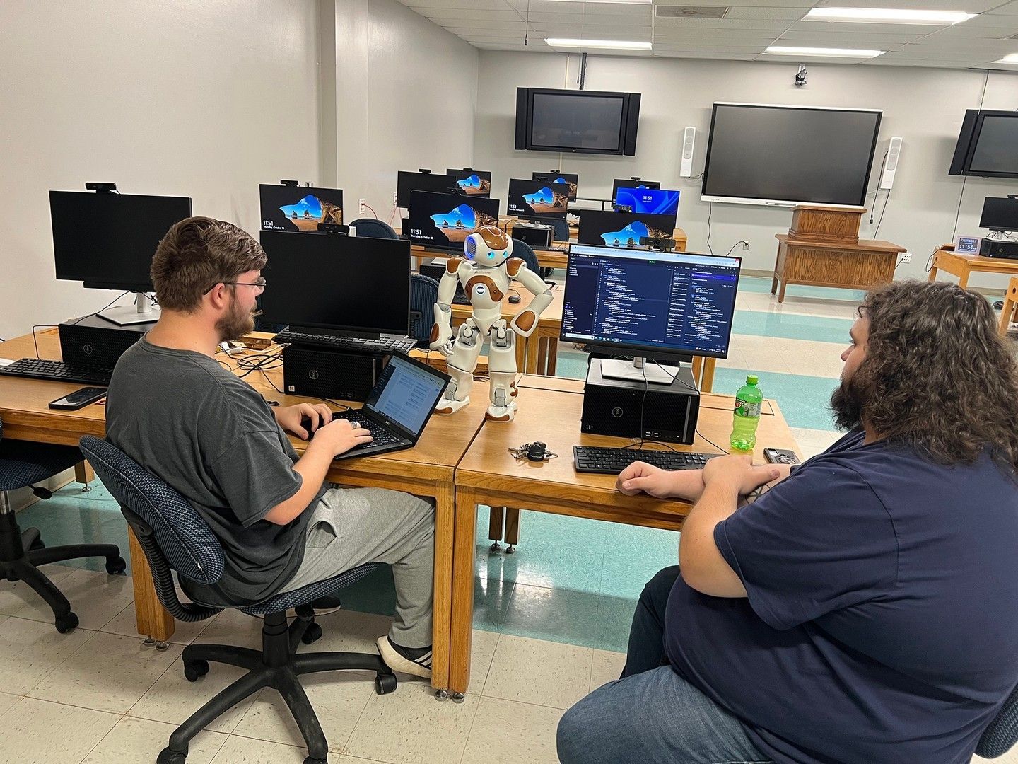 Two men are sitting at desks in a computer lab.
