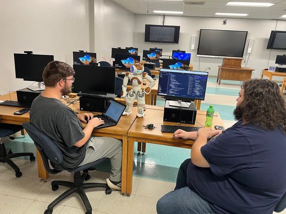 Two men are sitting at desks in a computer lab.