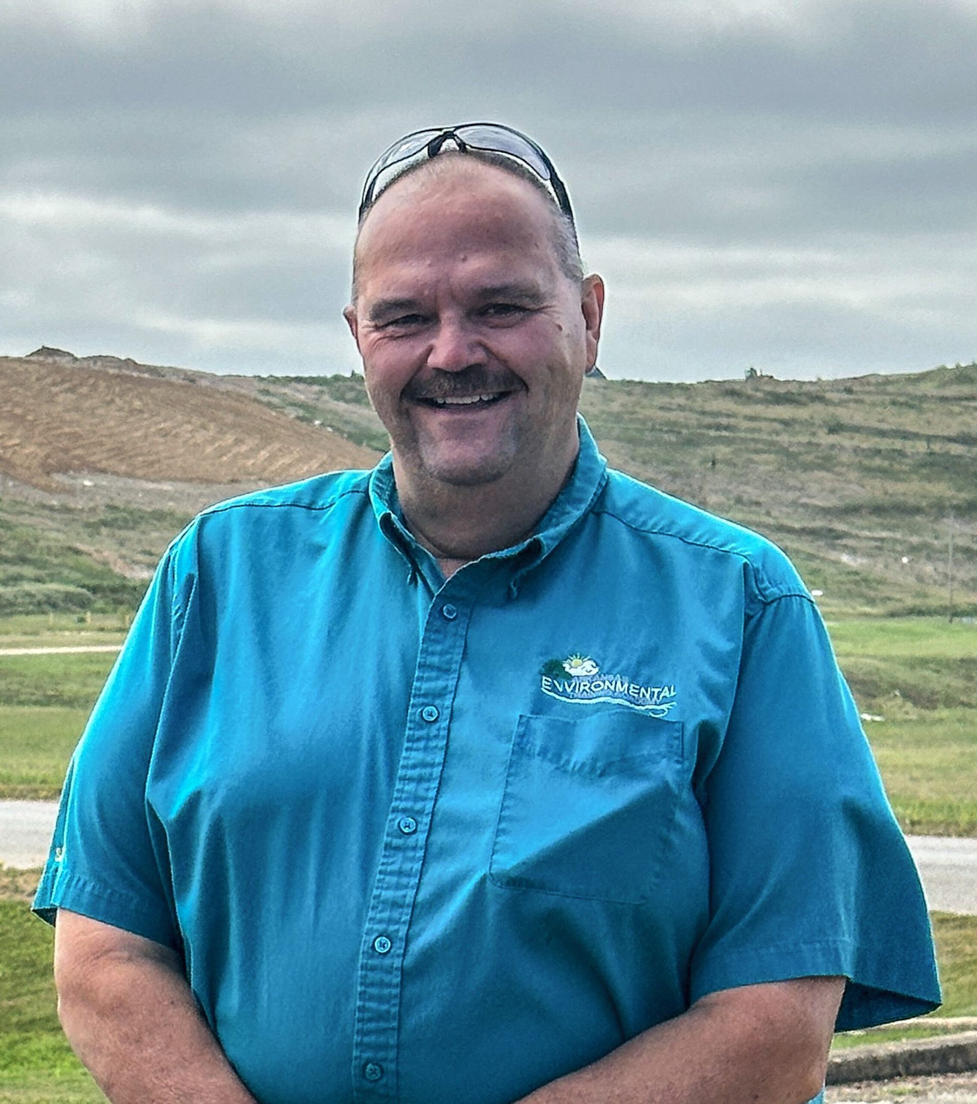 A man wearing a blue shirt and sunglasses is standing in a field.