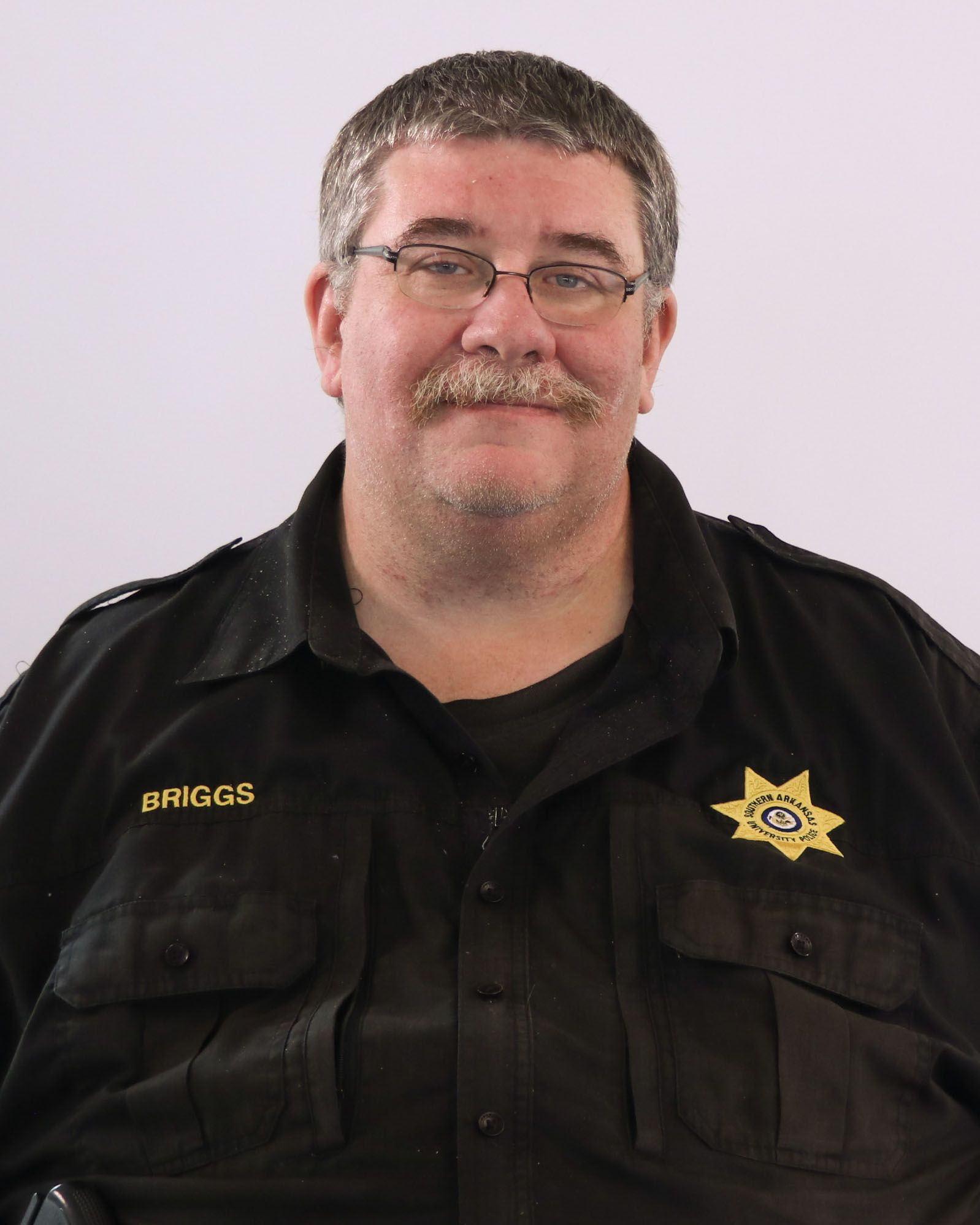 A man with glasses and a mustache is wearing a black shirt with the name biggs on it