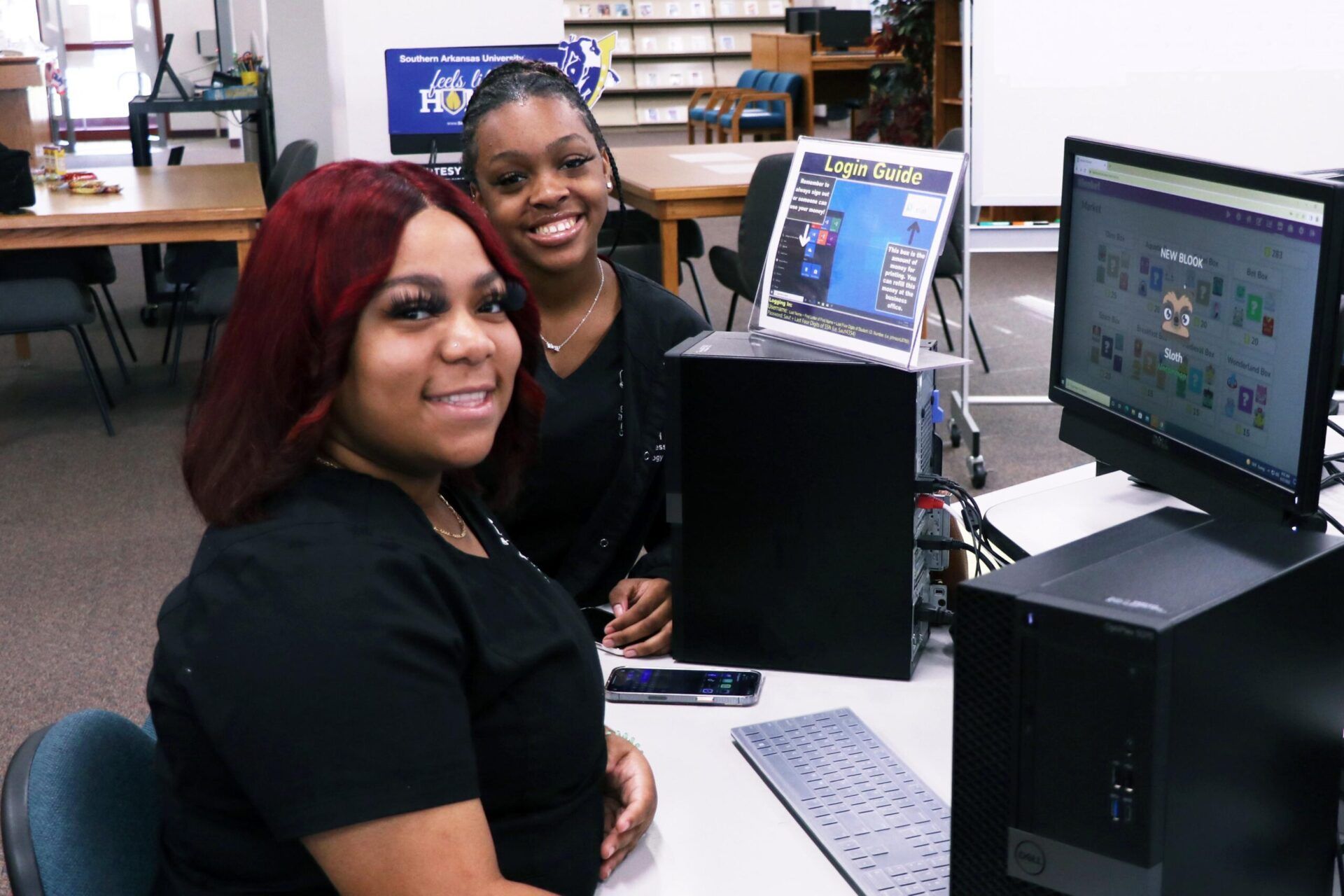 Two women are sitting at a desk in front of a computer.