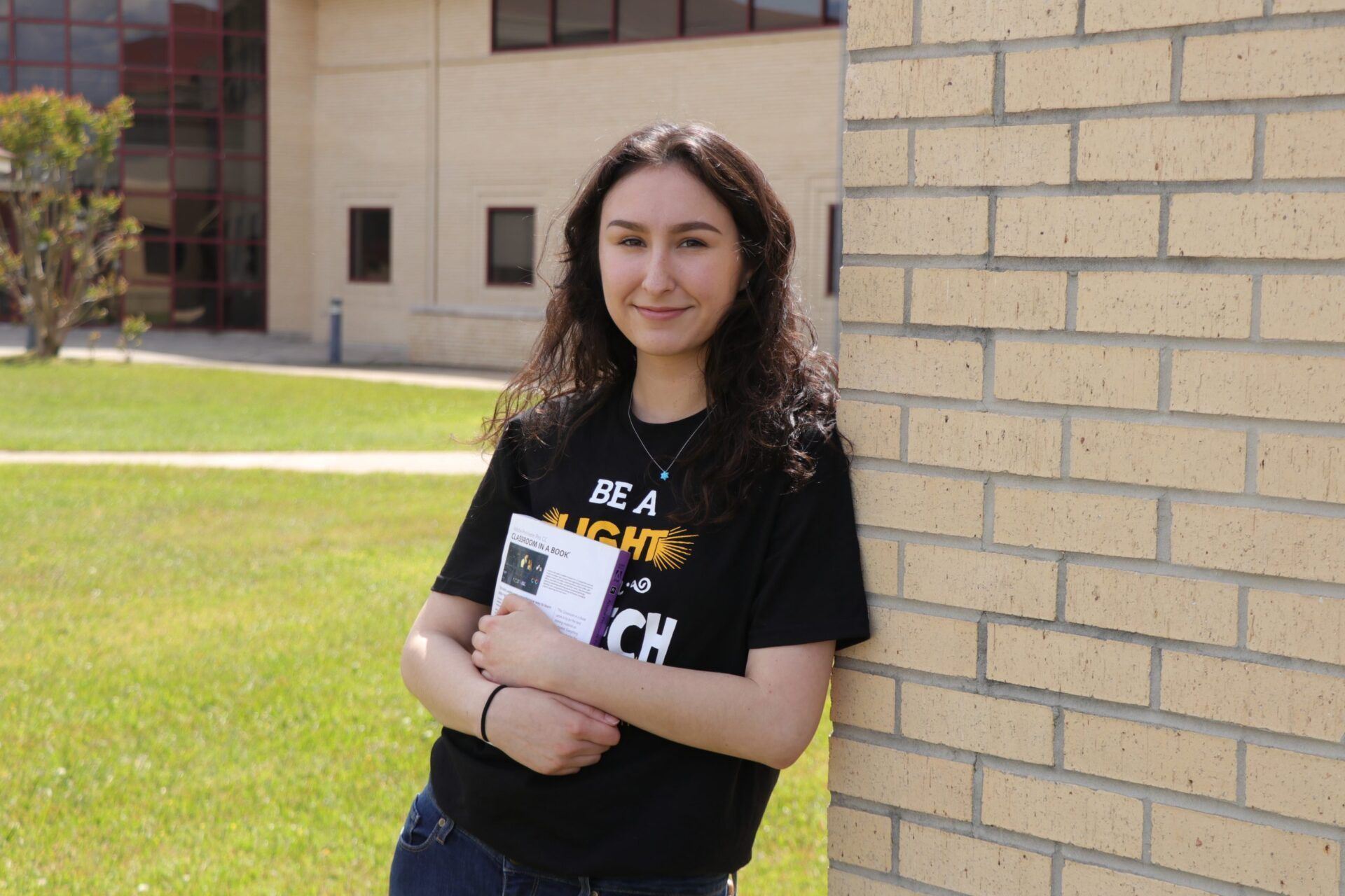 A woman is leaning against a brick wall while holding a book.
