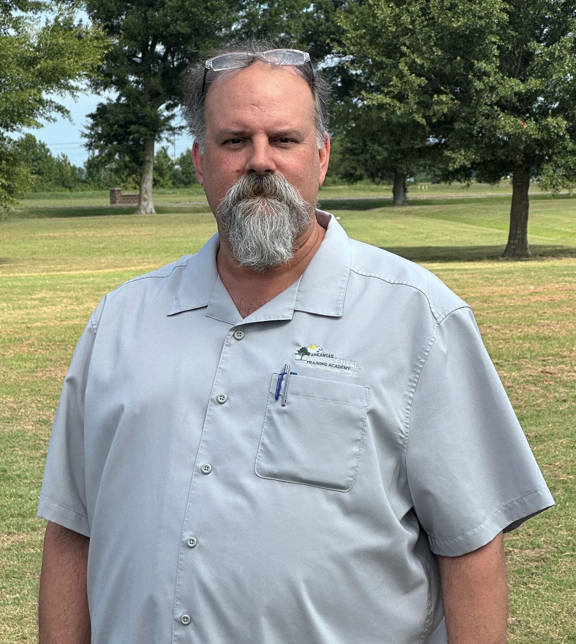 A man with a beard and sunglasses is standing in a park.