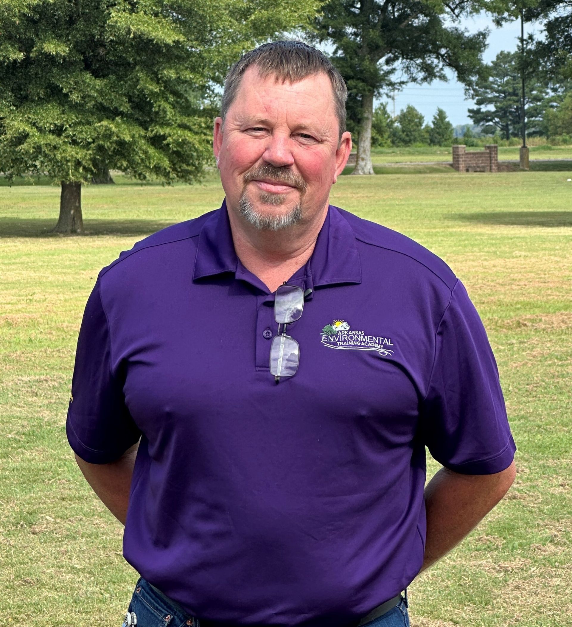 A man in a purple shirt is standing in a grassy field.
