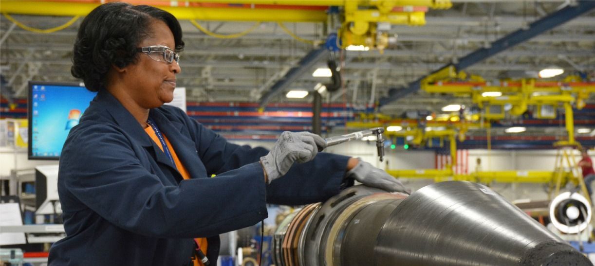 A woman is working on a piece of metal in a factory.