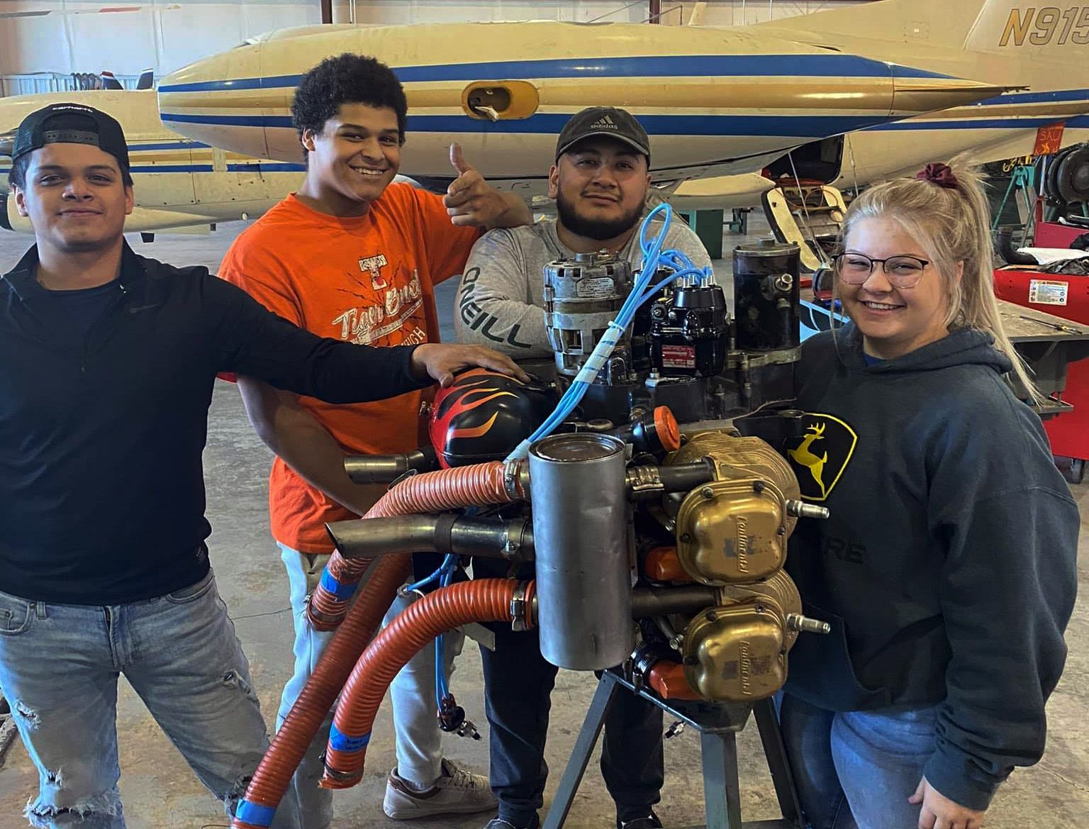 A group of people are posing for a picture in front of an airplane engine.