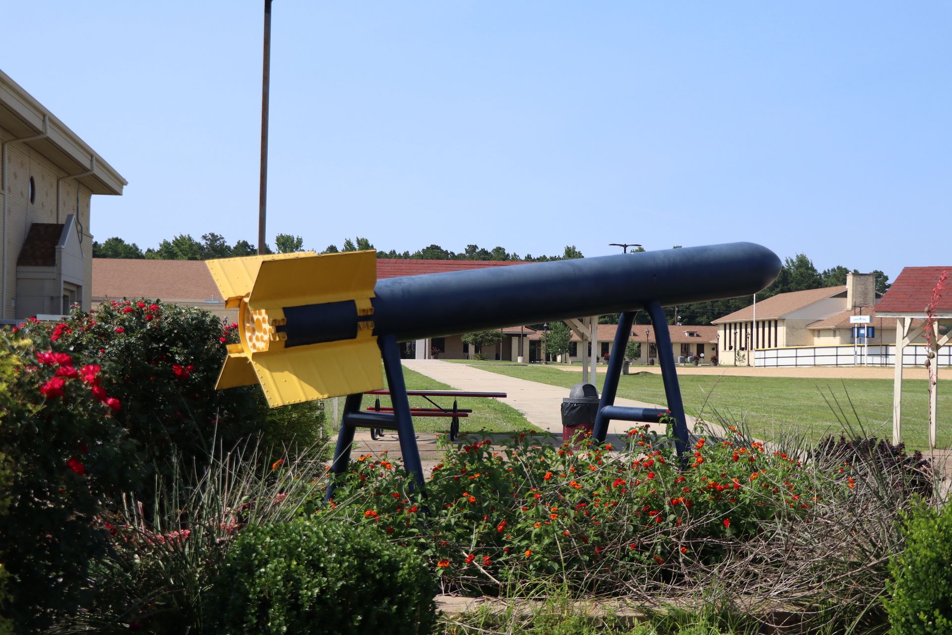 A yellow and black rocket is sitting in a garden in front of a building.