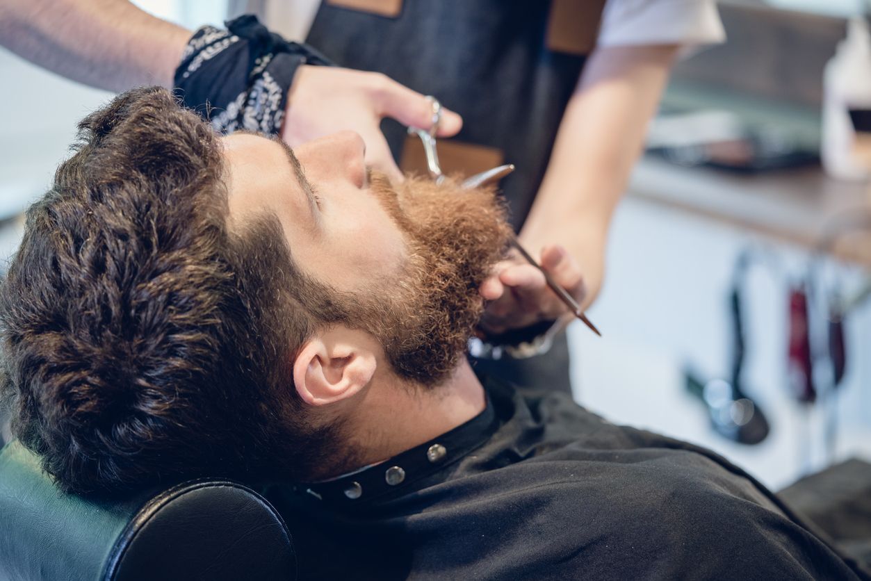 A man is getting his beard shaved by a barber in a barber shop.