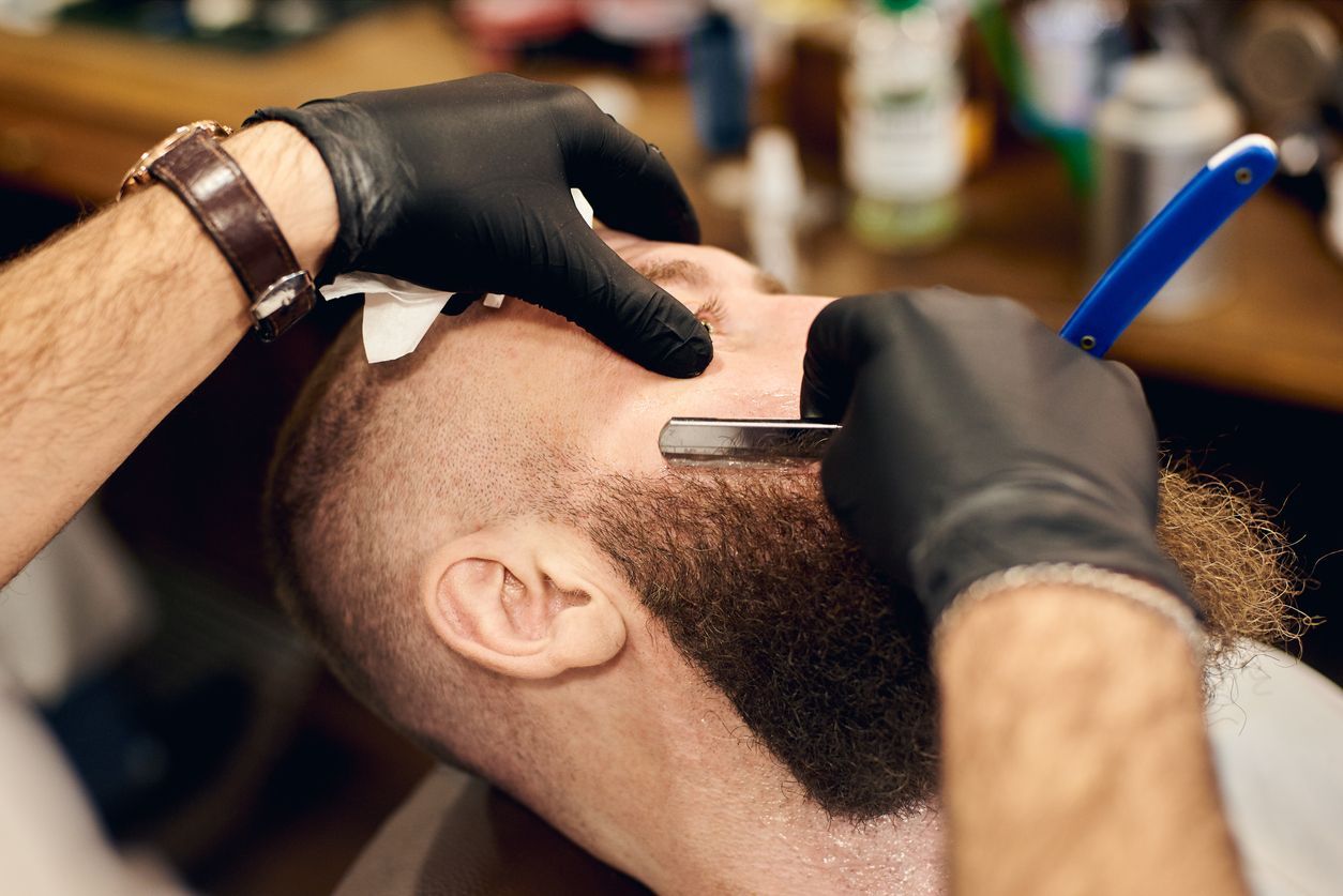 A man is getting his beard shaved by a barber in a barber shop.