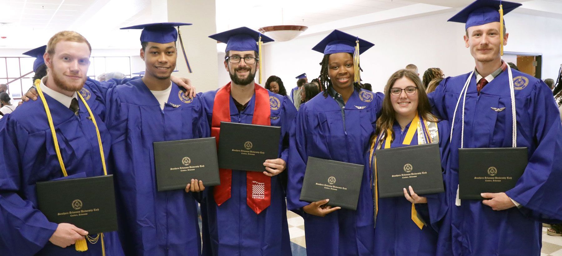 A group of graduates are posing for a picture while holding their diplomas.