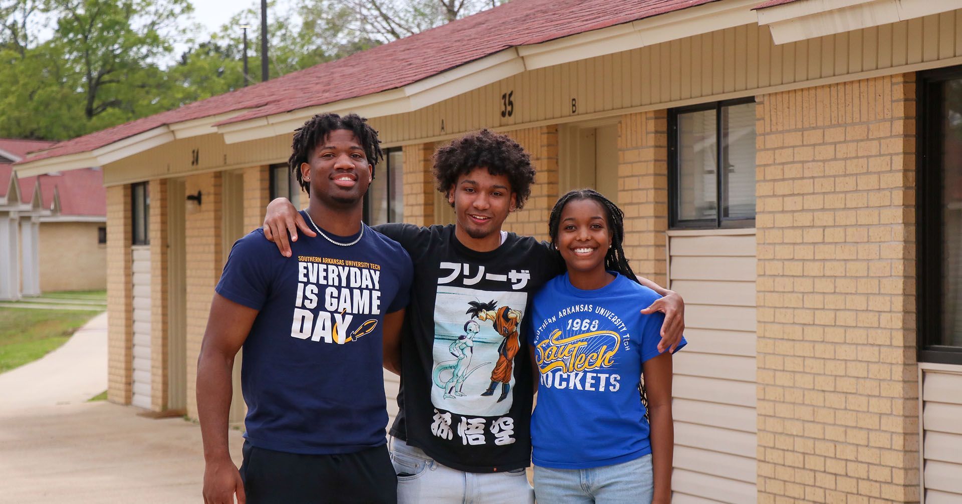 Three young people are posing for a picture in front of a brick building.