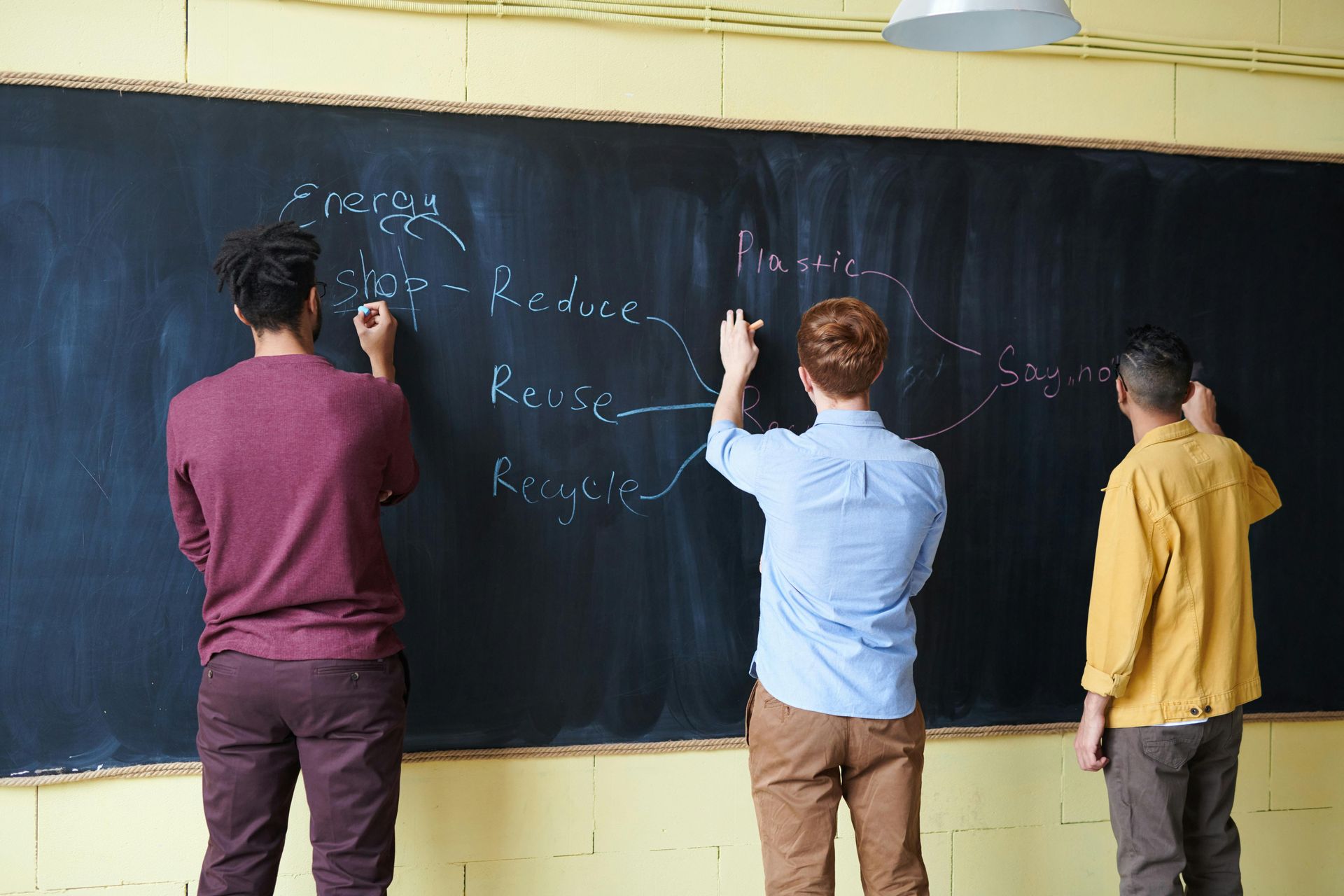 Three men are writing on a blackboard in a classroom