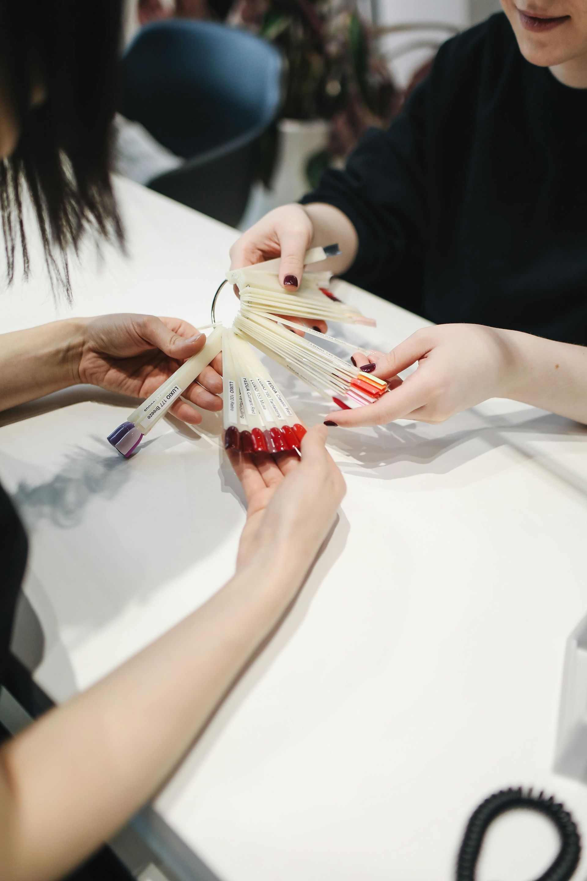 A woman is sitting at a table holding a bottle of nail polish.