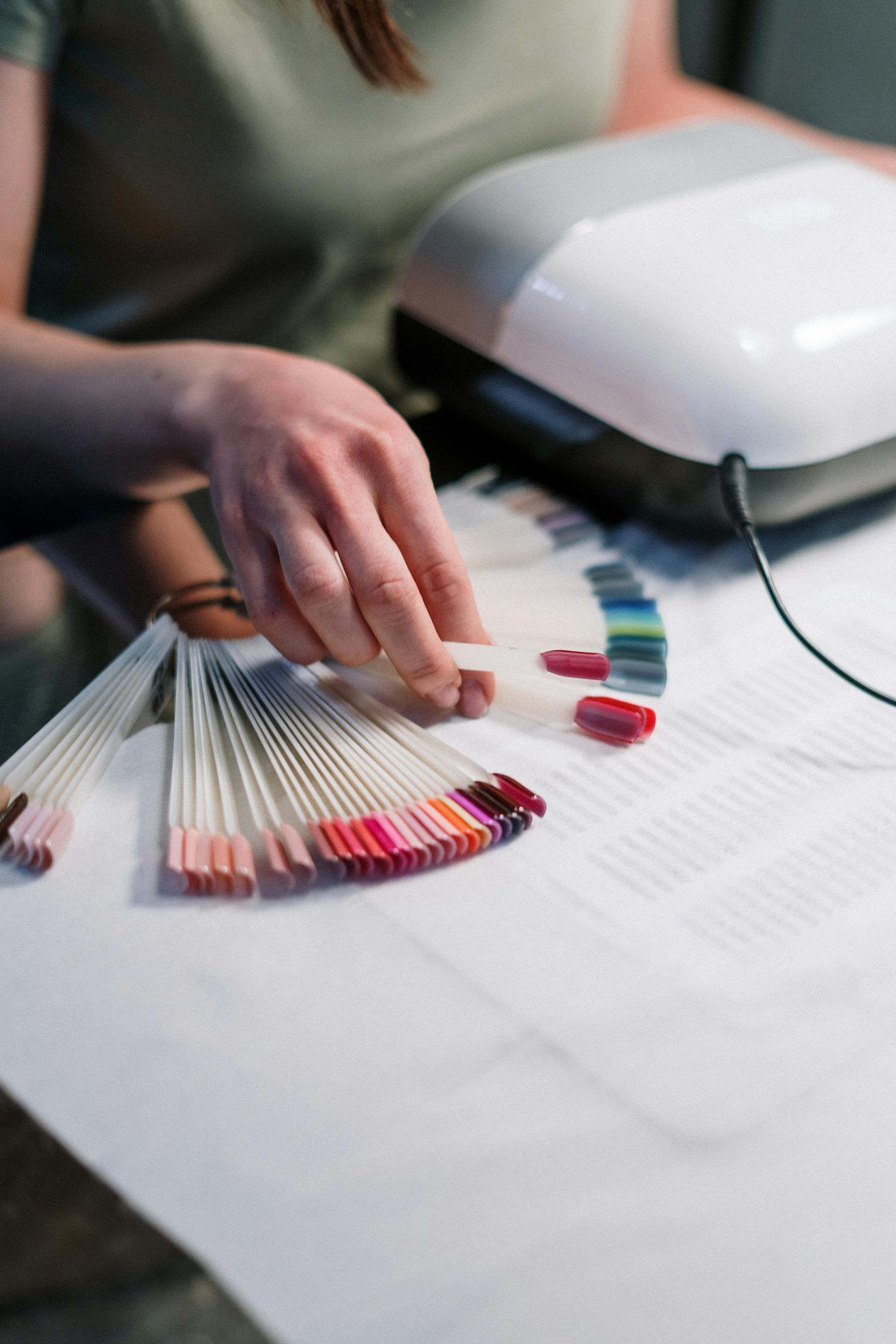 A woman is sitting at a table with a bunch of samples of nail polish.