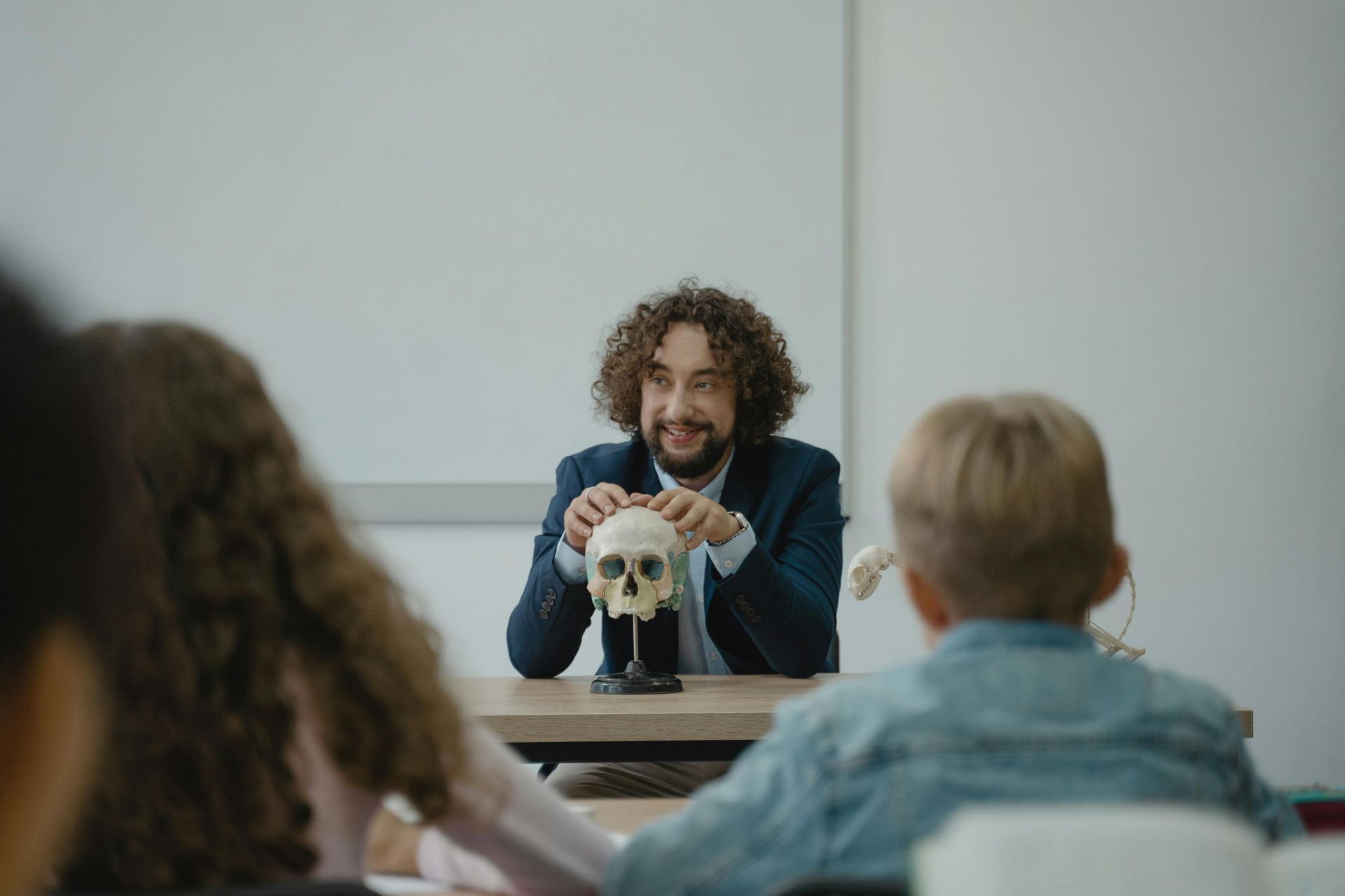 A man is holding a model of a skull in front of a group of children in a classroom.
