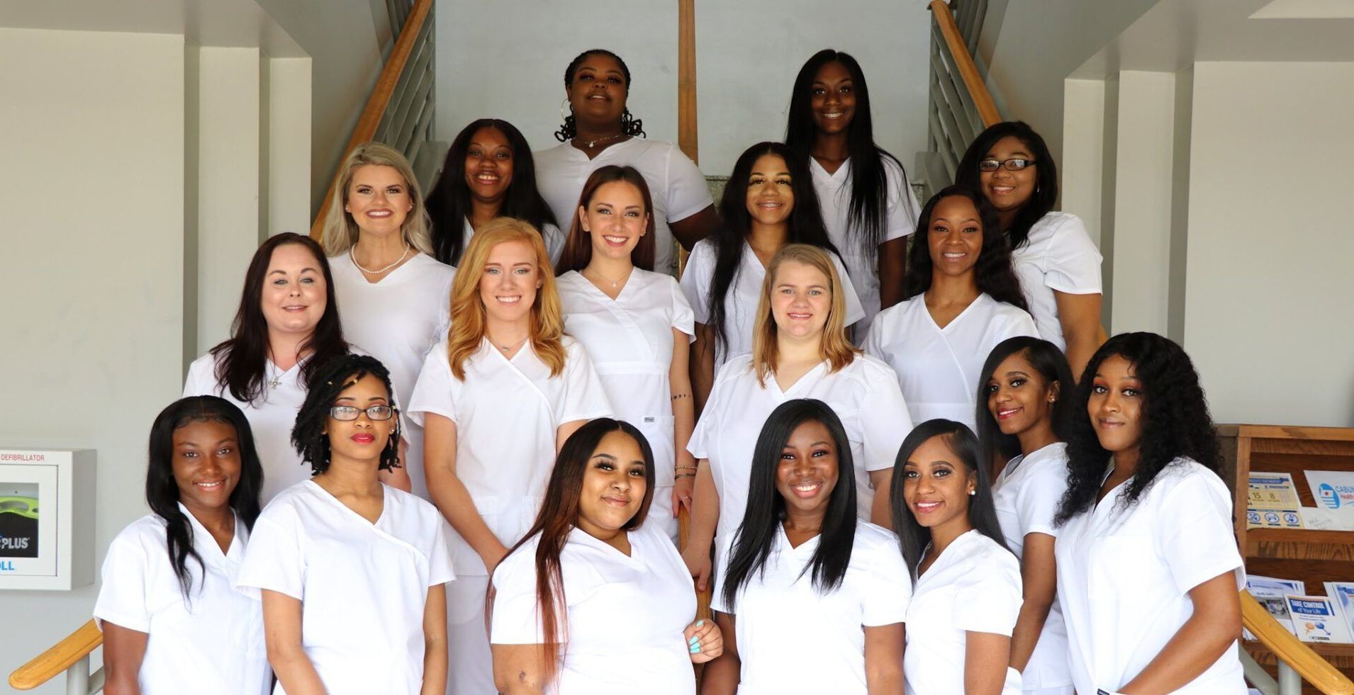 A group of women in white scrubs are posing for a picture on a set of stairs.