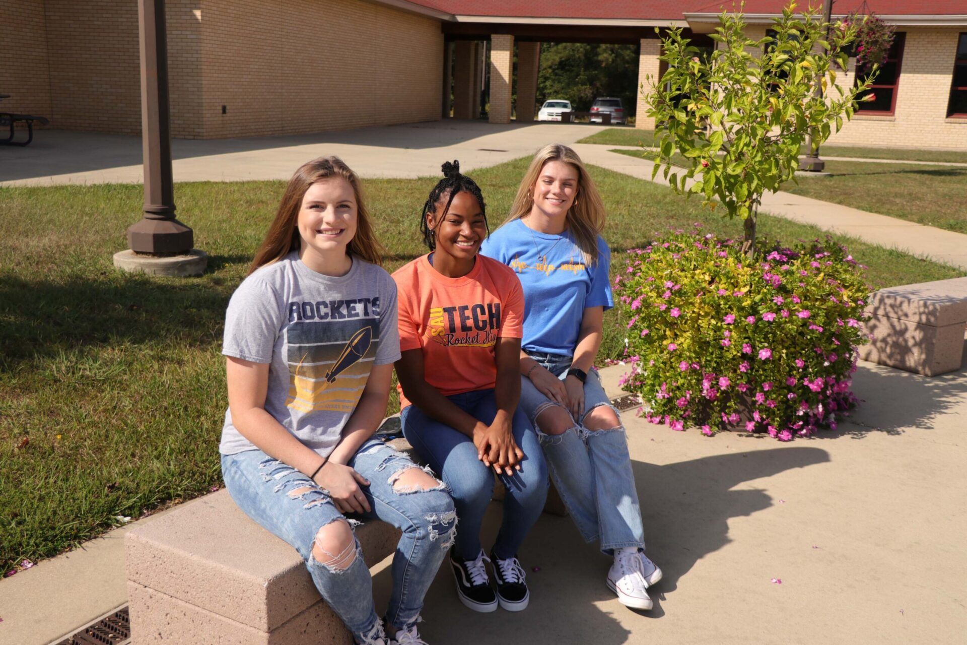 Three girls are sitting on a bench in front of a building.