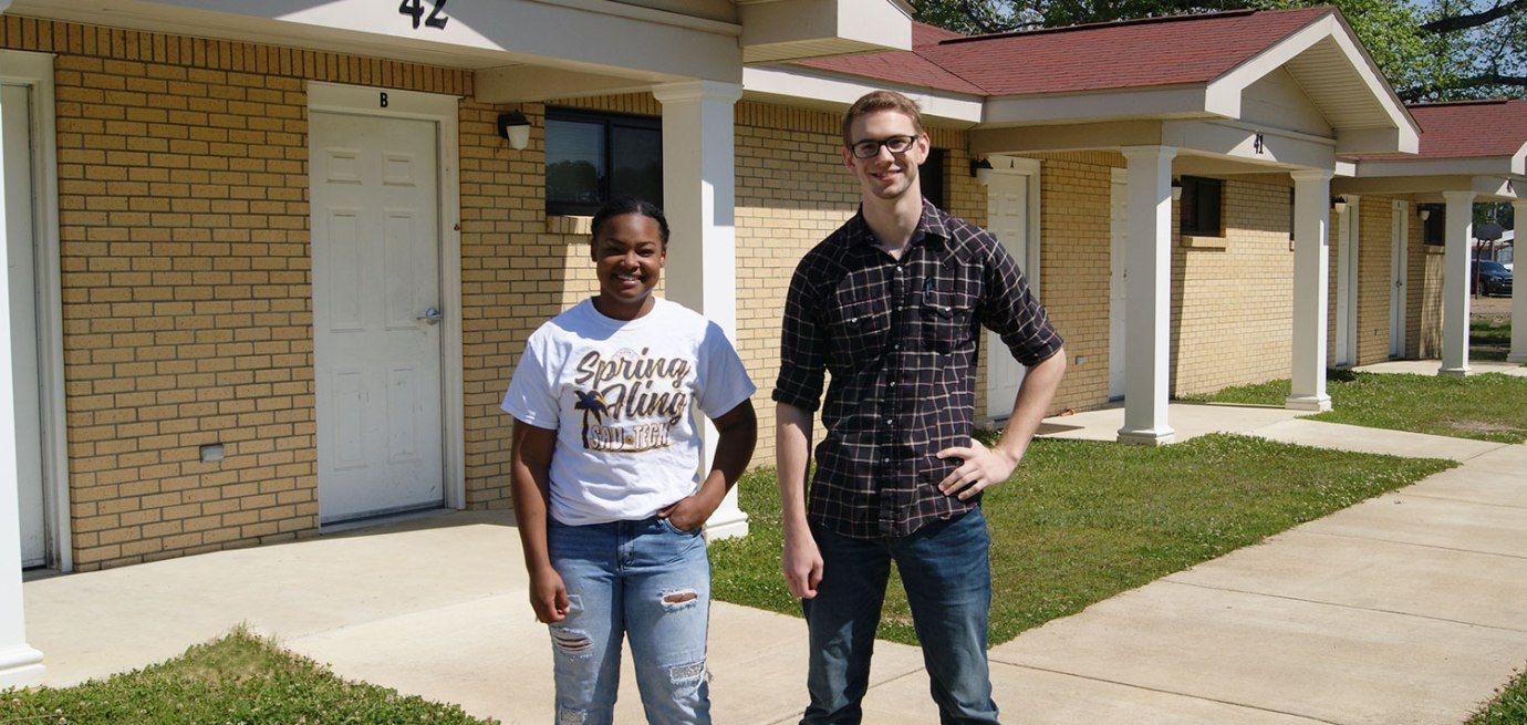 A man and a woman are standing in front of a brick building.