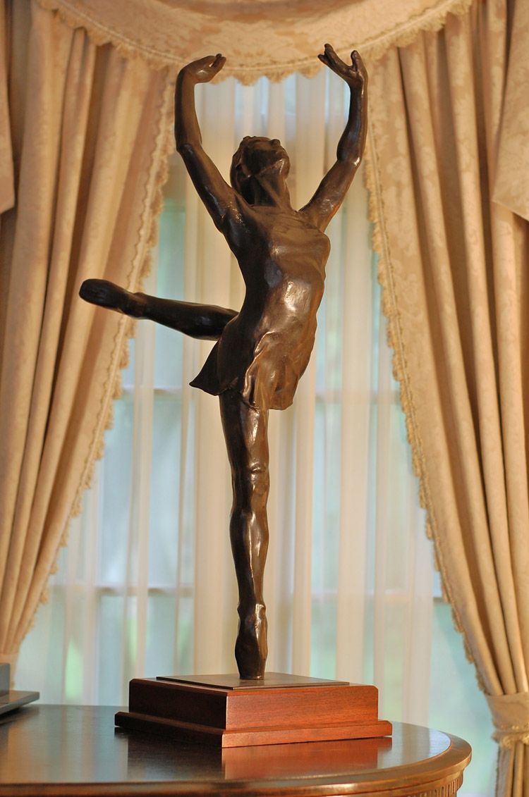 A statue of a ballerina is sitting on a table in front of a window.