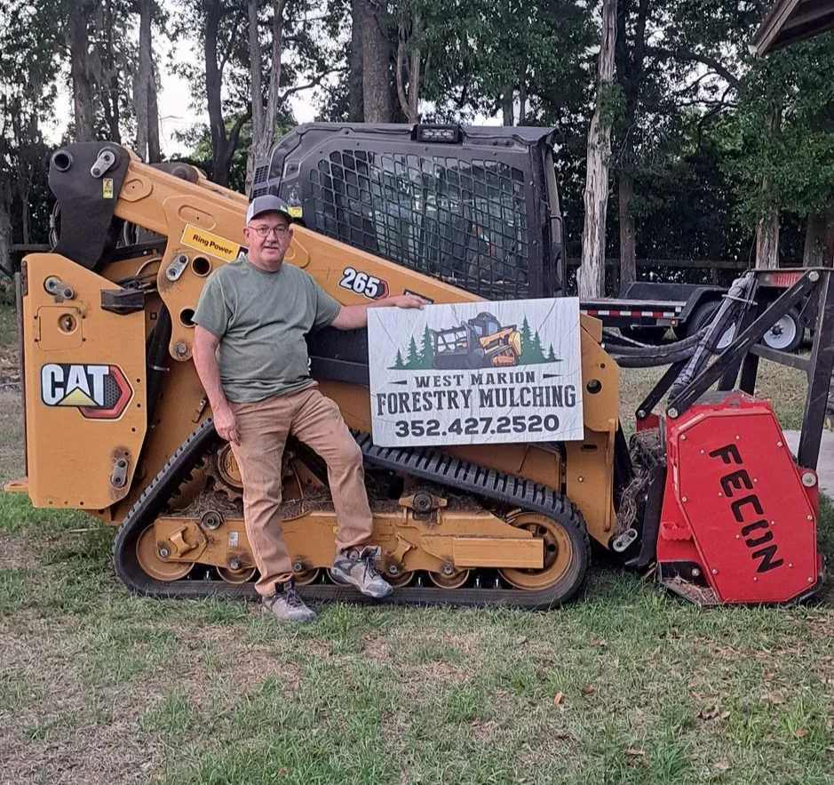 Orange and black track skid steer mulching near a tree, kicking up wood chips.