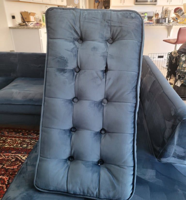 A vertical, rectangular blue velvet tufted cushion with ten buttons, resting on a matching sofa in a living room.