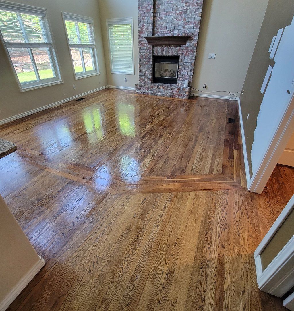 A high-angle view of a living room featuring polished hardwood floors, large windows, and a brick fireplace.
