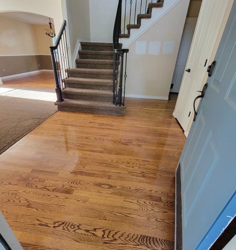 An entryway featuring light-colored hardwood flooring, a staircase with carpeted steps, and a blue-painted front door.