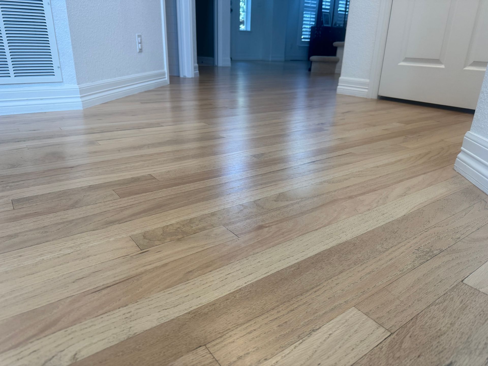 Person sanding a wooden floor with a floor sander in an interior room.