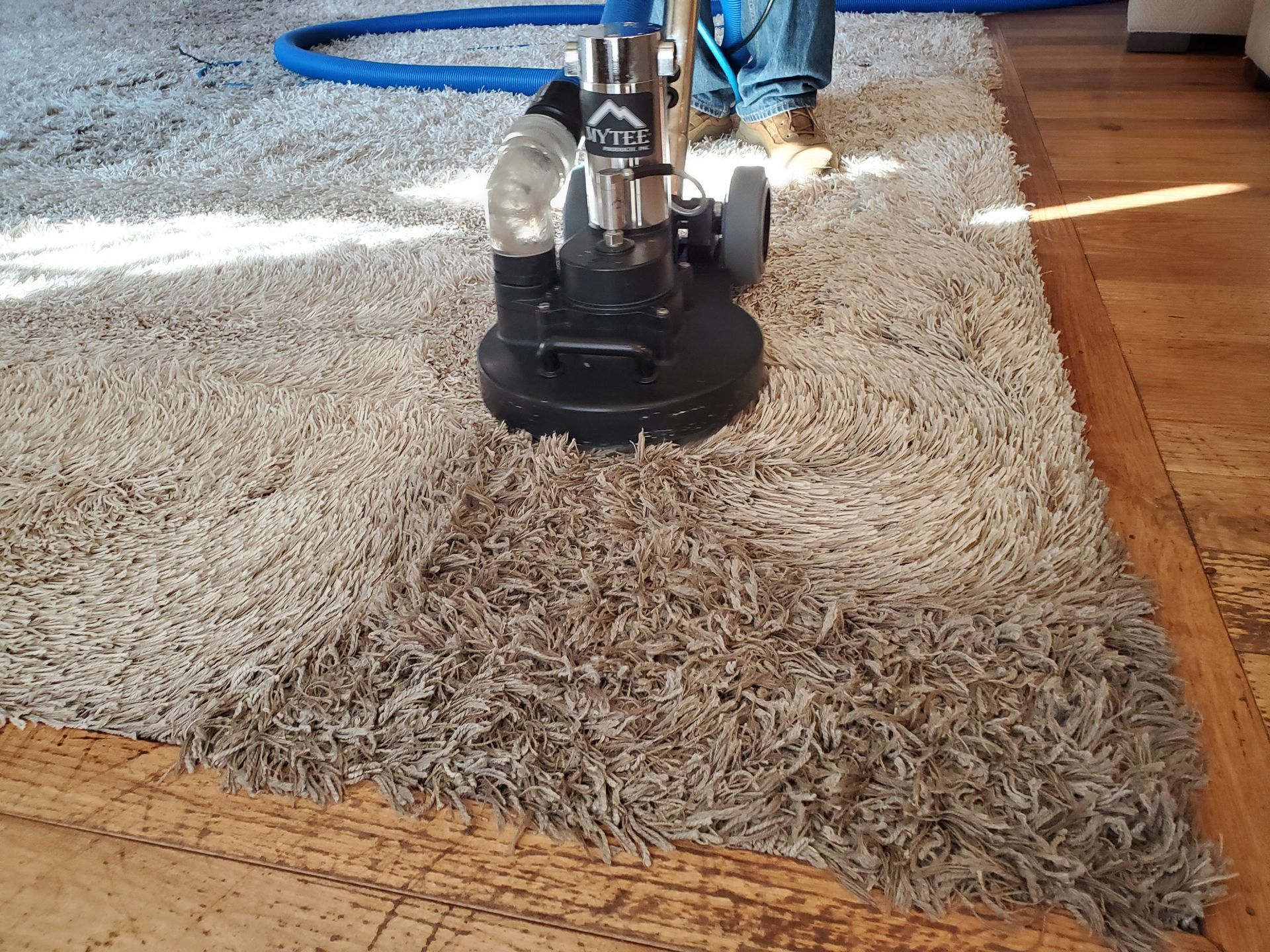Handheld carpet cleaner cleaning a brown and beige striped rug.