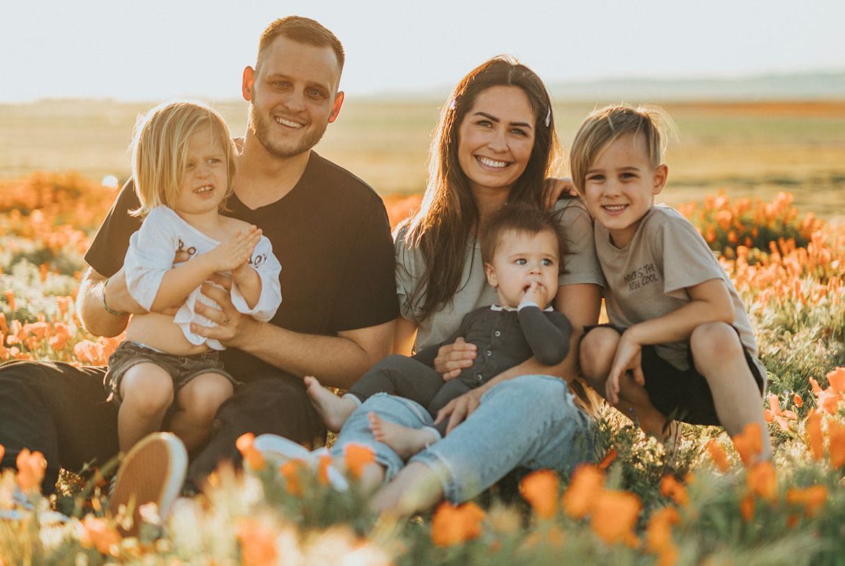 A family of five sitting together in a field of orange flowers under warm, golden sunlight.