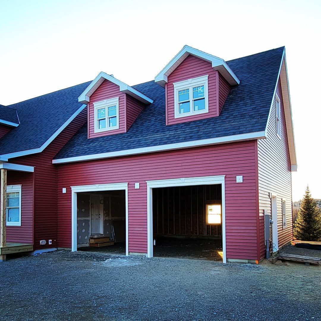 A red house with a black roof and two garage doors