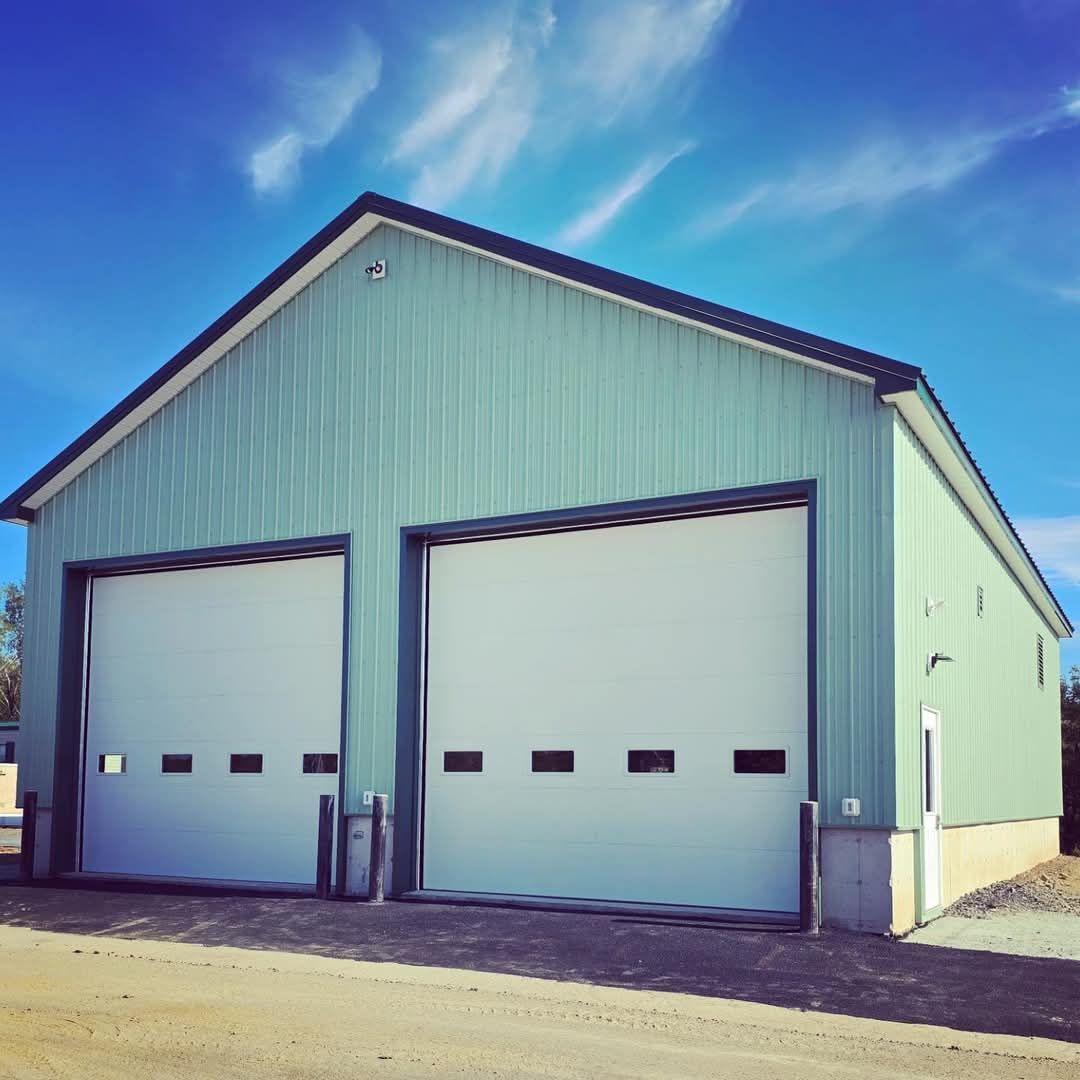 A green building with white garage doors on a sunny day