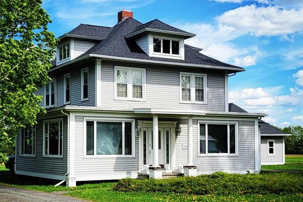 A large white house with a black roof is sitting on top of a lush green field.