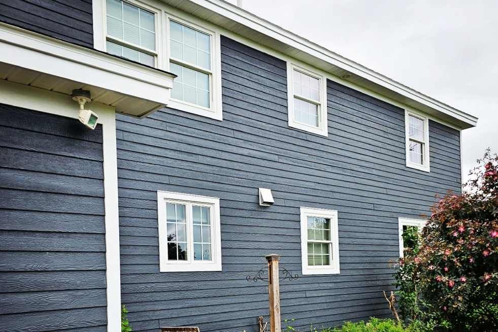 A large house with a blue siding and white trim has a mailbox in front of it.