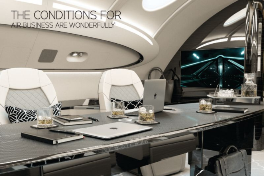 Interior of a luxury private jet with a table, drinks, laptops, and seating. Text reads, 